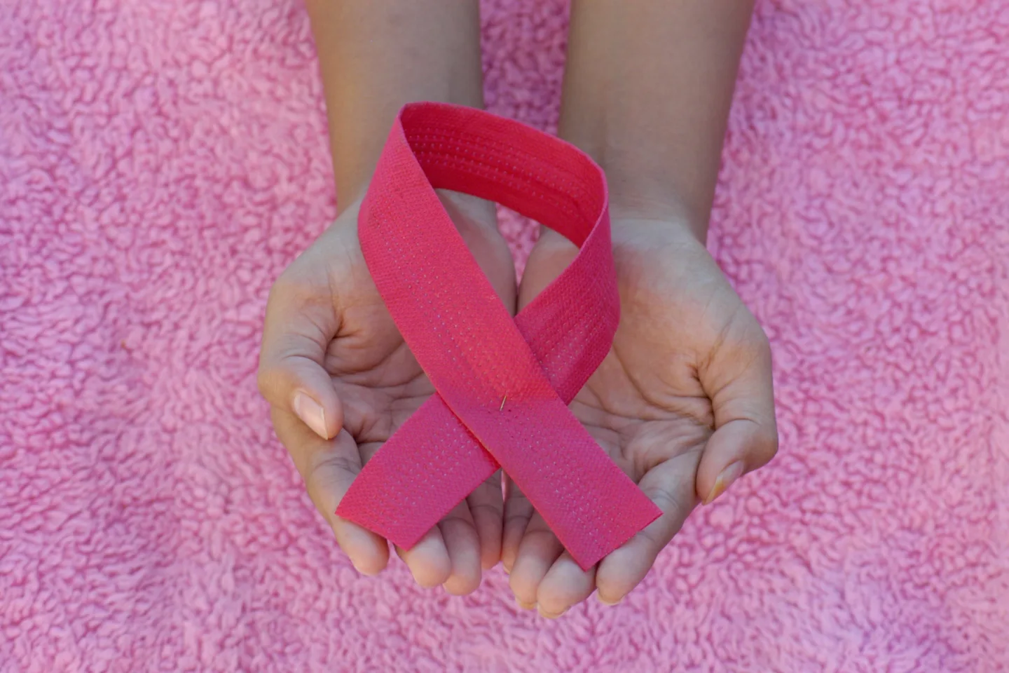 Hands holding a pink breast cancer awareness ribbon